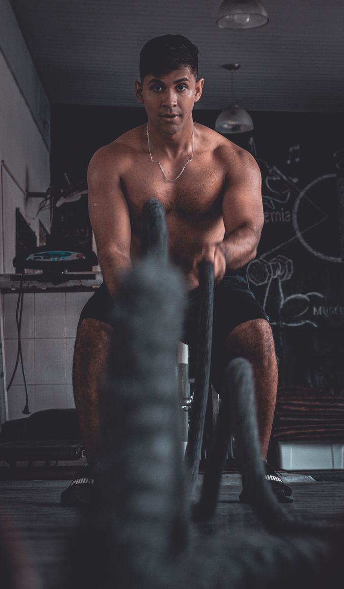 gallery-1 Fit young man working out with battle ropes in a gym setting.