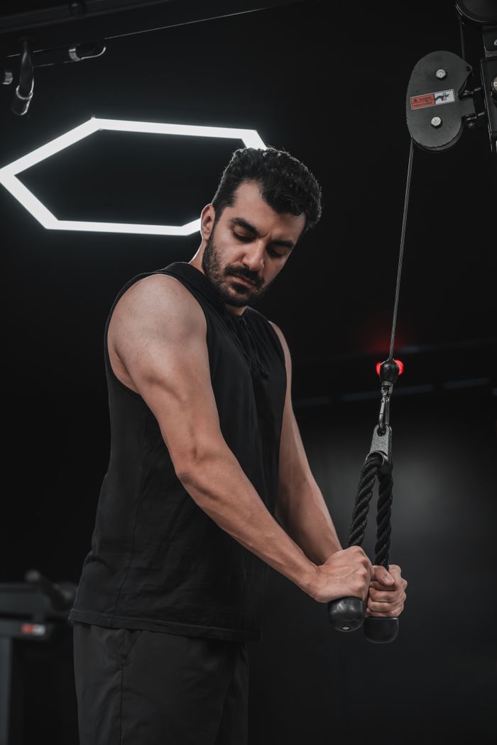 gallery-6 A focused adult male exercising using a cable machine in a modern gym setting.