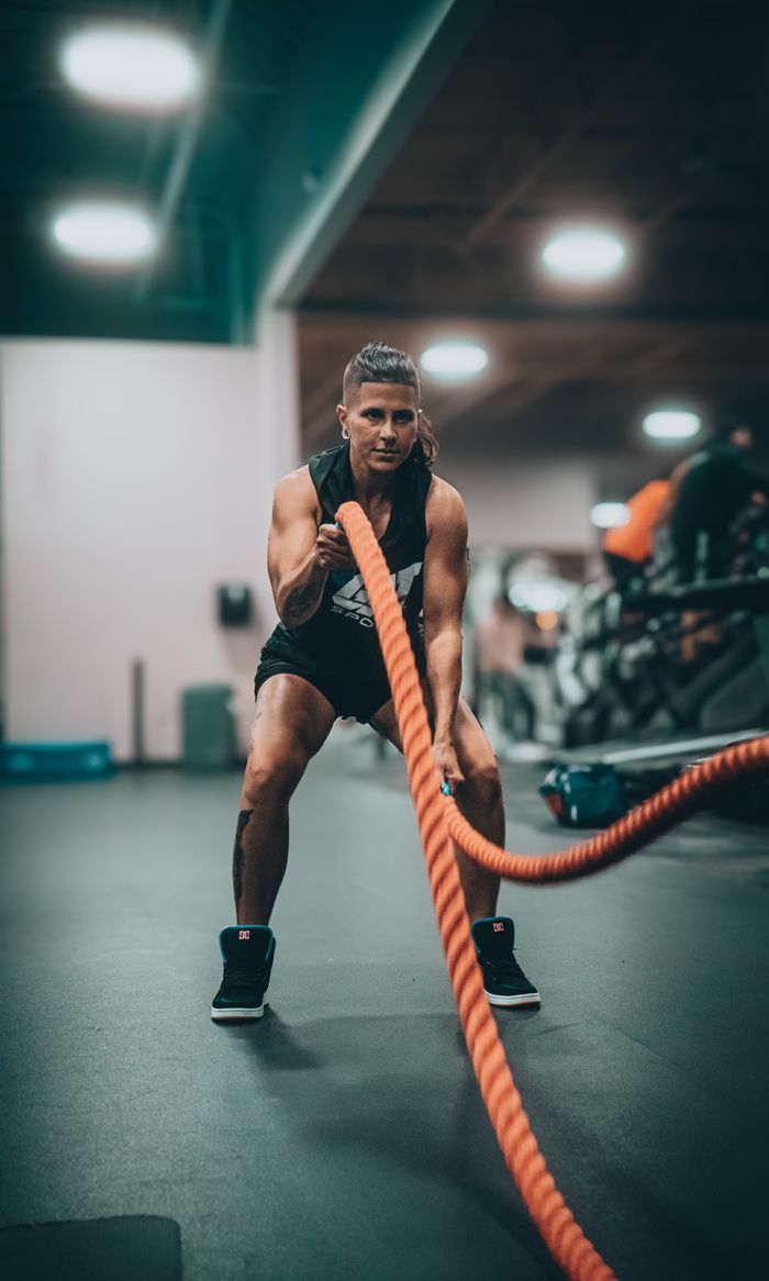 services-02 Athletic person performing an intense battle rope exercise in a modern gym setting.